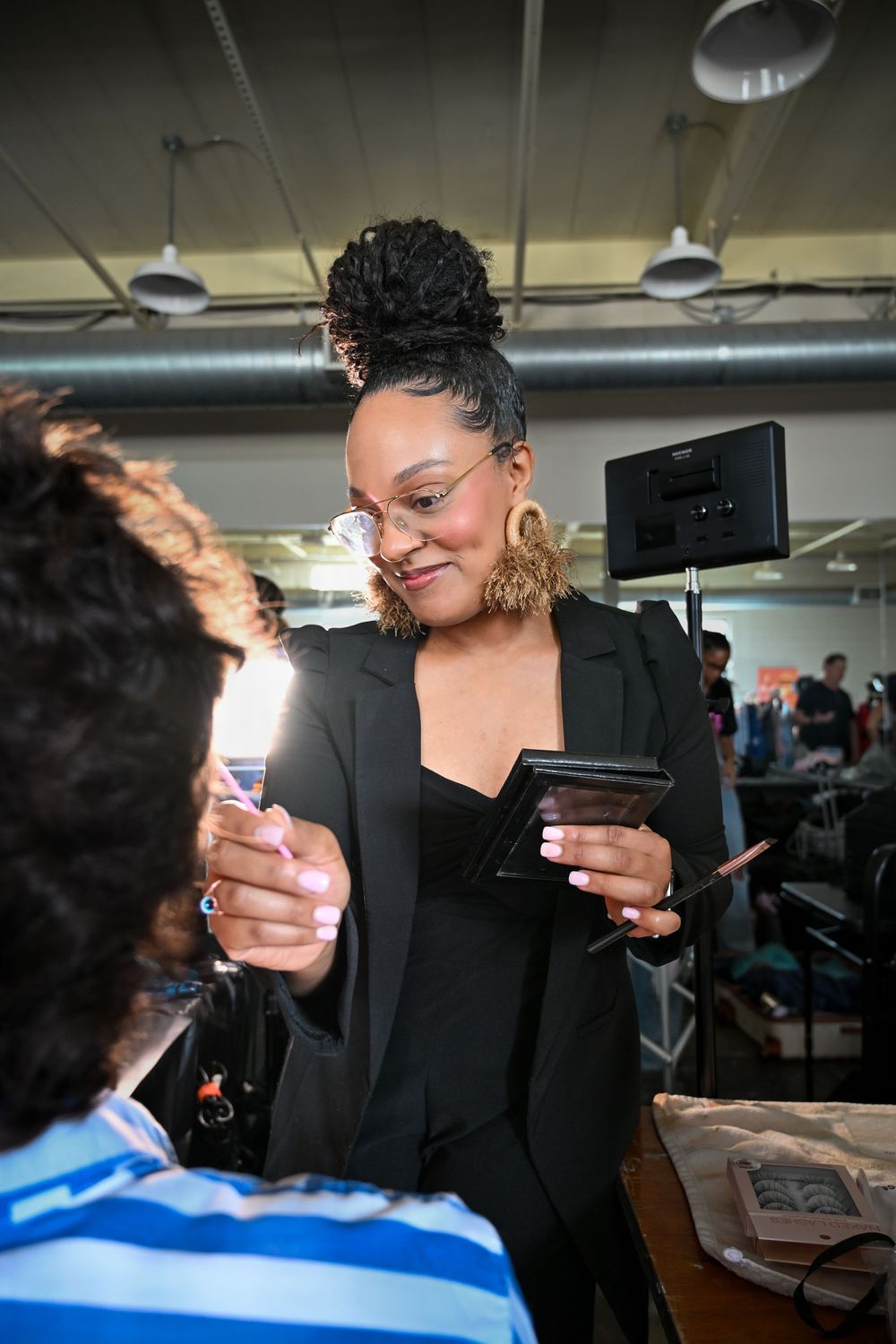 Makeup artist in black blazer holding cosmetics and credit card while working at beauty counter.