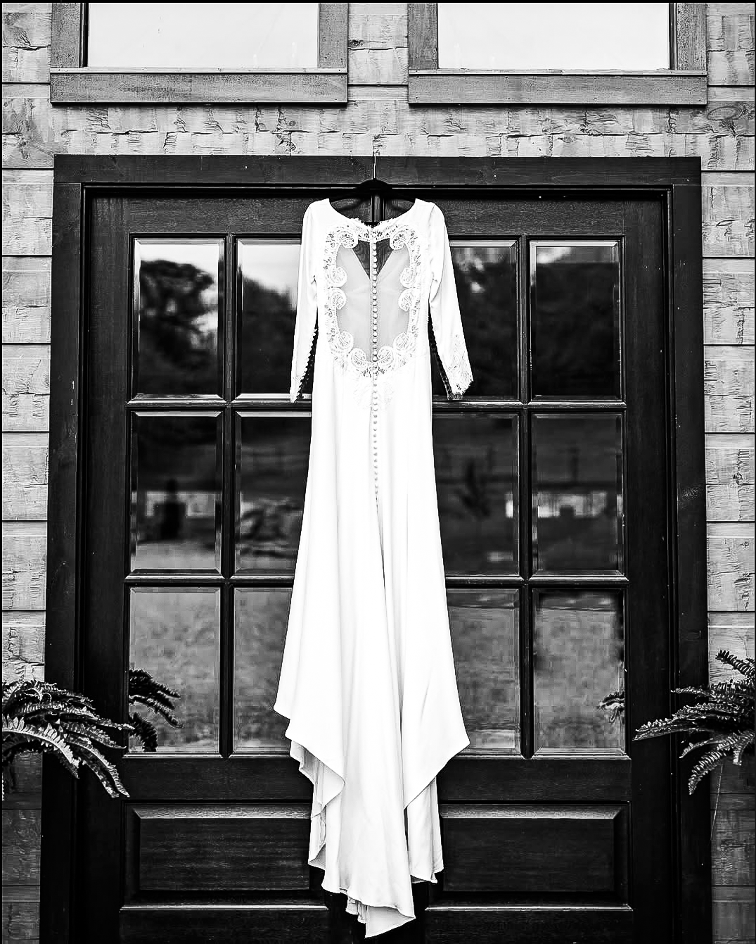 Elegant white wedding dress hanging on black window frame with dramatic lighting.