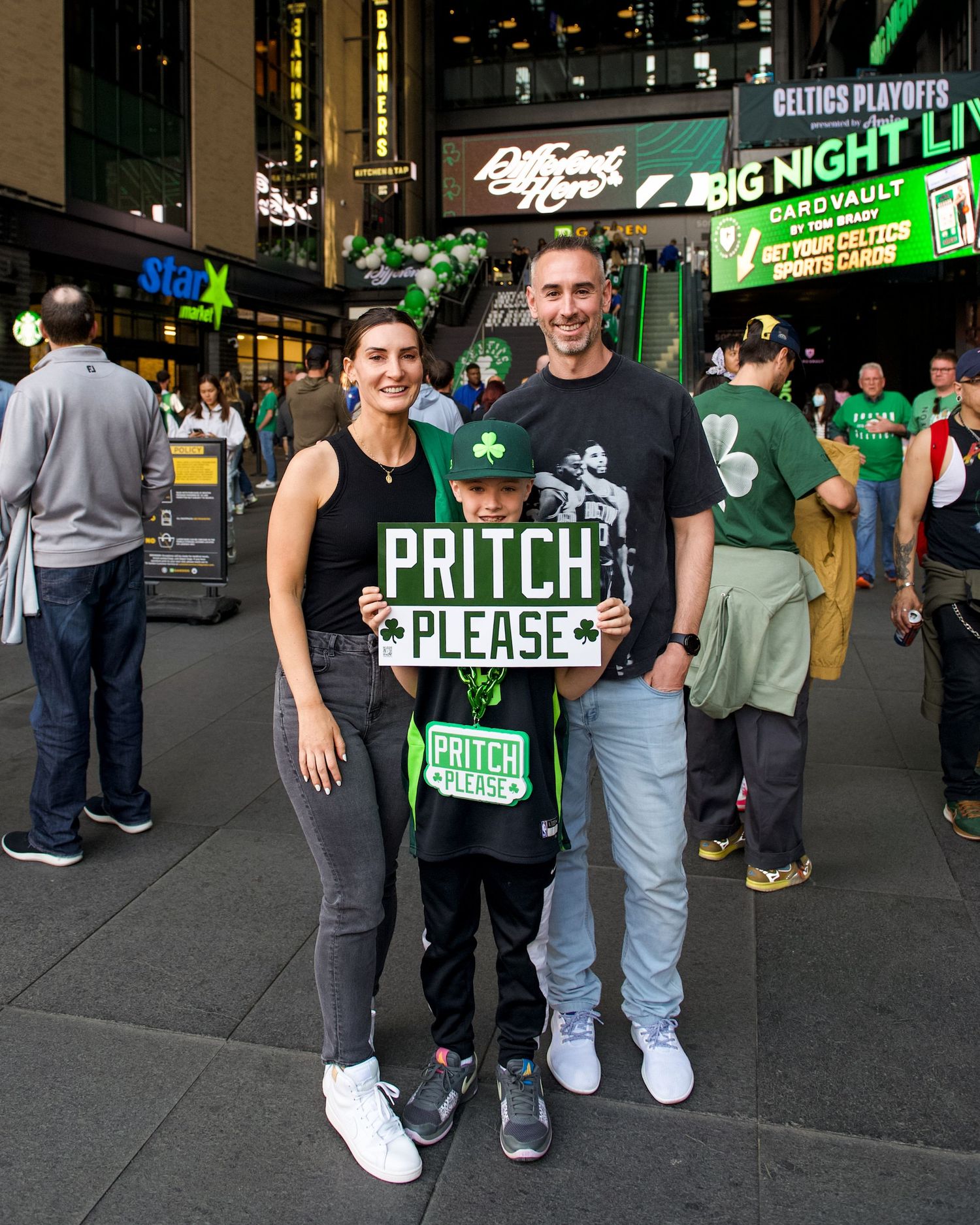Celtics basketball fans wearing team merchandise pose with a 'Pritch Please' sign outside TD Garden in Boston.