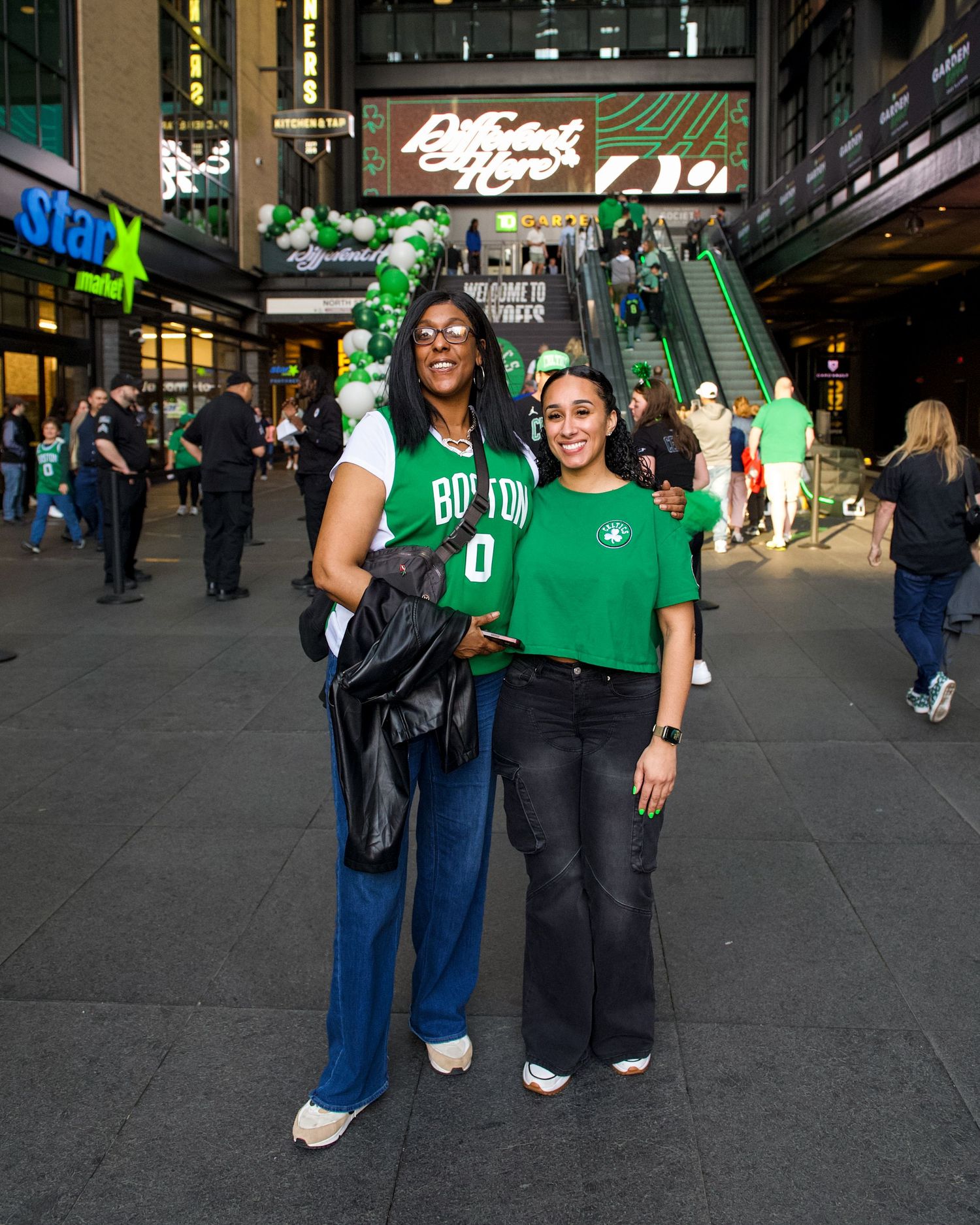 Two basketball fans wearing green jerseys pose together outside TD Garden in Boston during game day festivities.