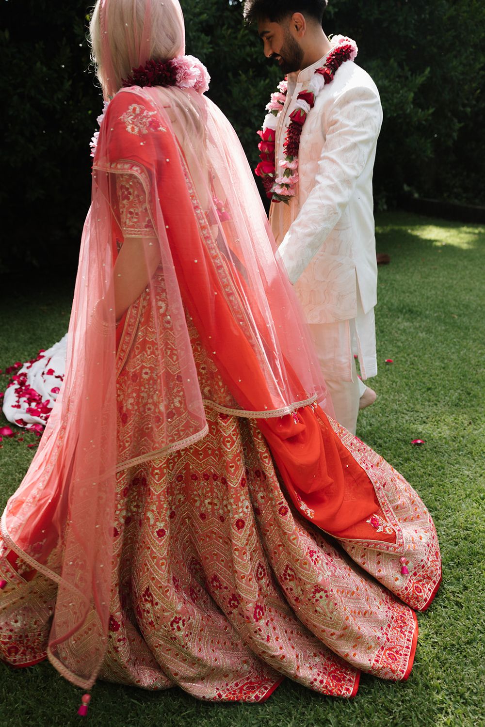 Close-up of ornate coral pink and gold Indian wedding lehenga with intricate embroidery details.