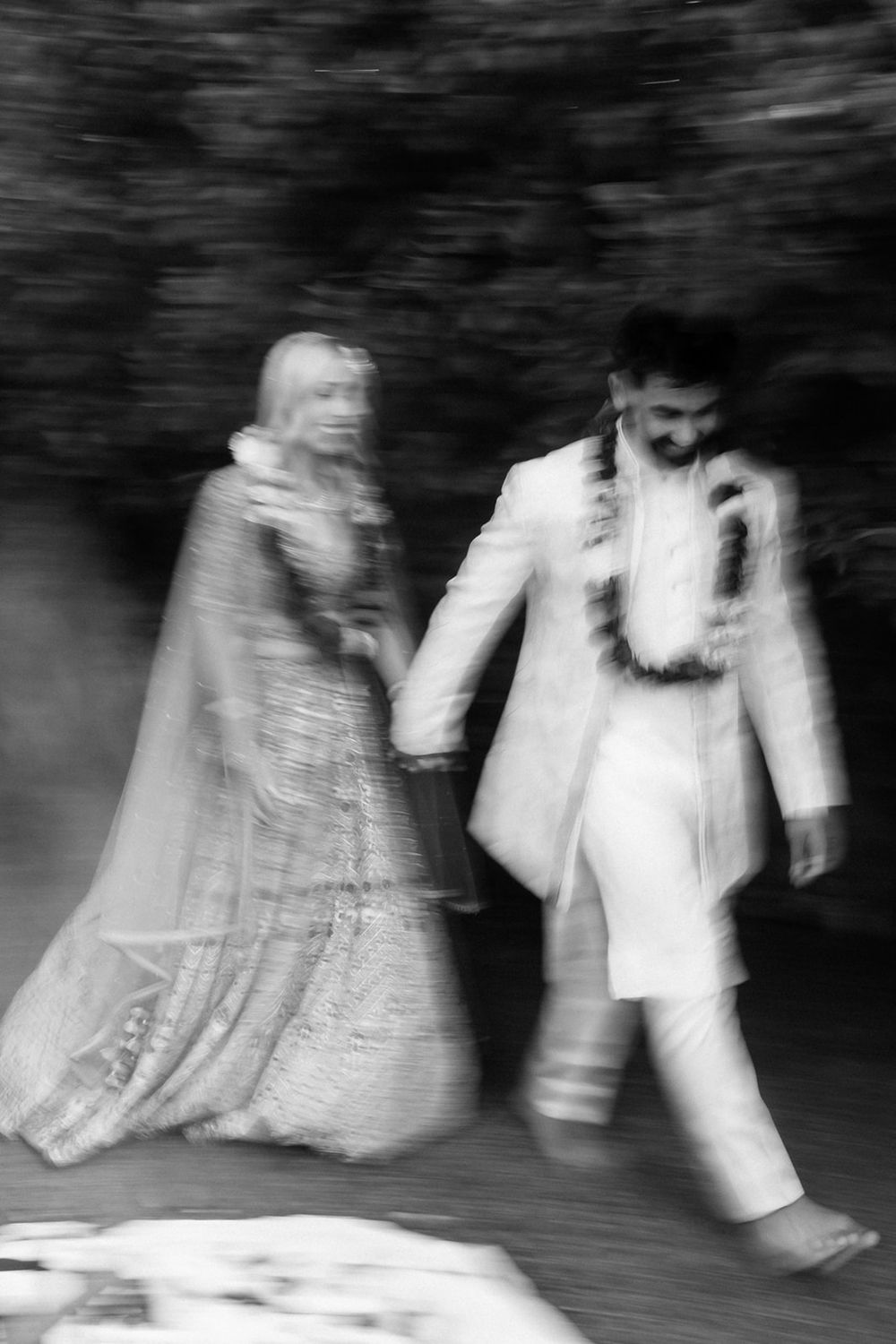 Artistic black and white motion blur photograph of a couple in traditional wedding attire walking together.