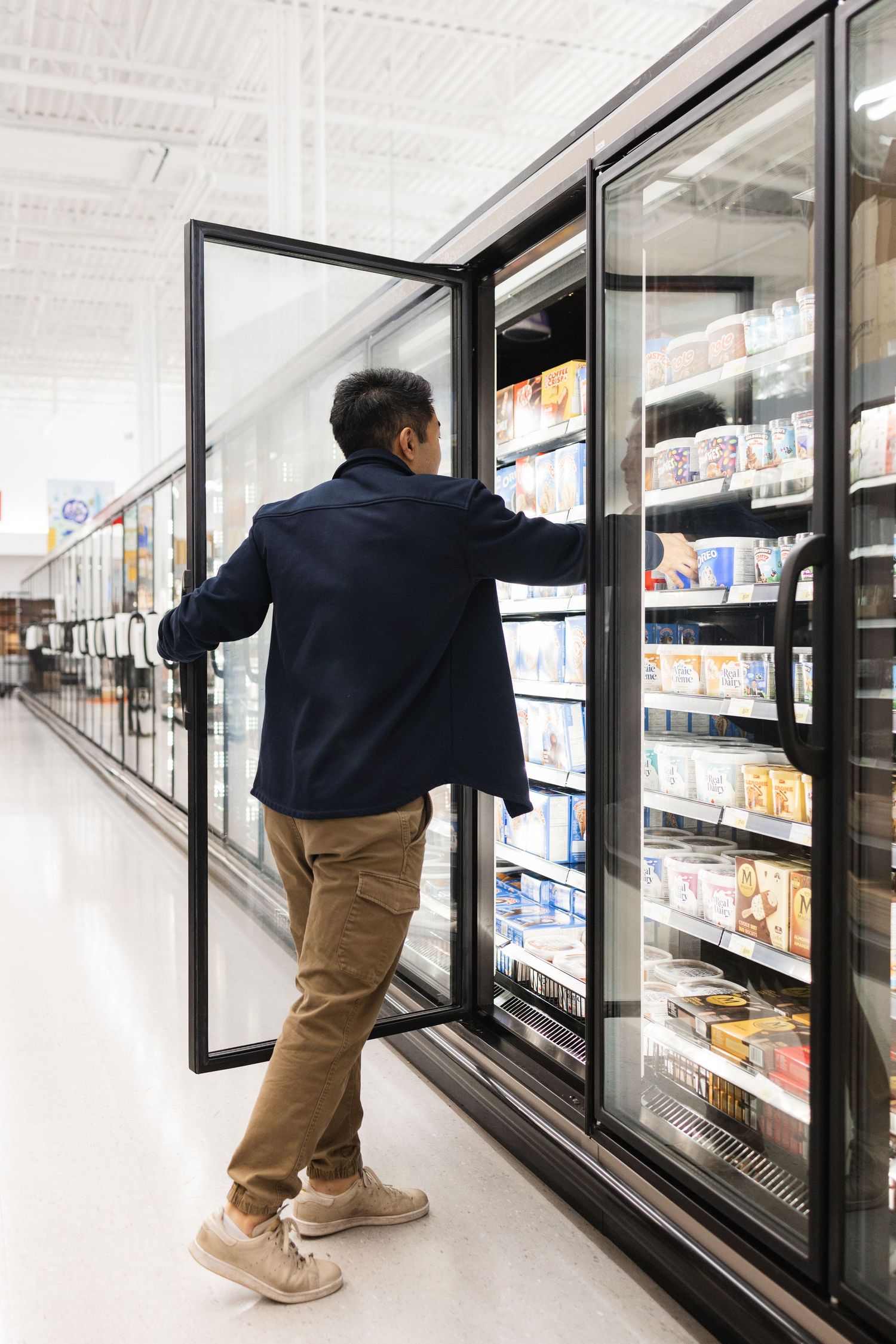 Person reaching into a commercial freezer display case at a grocery store.