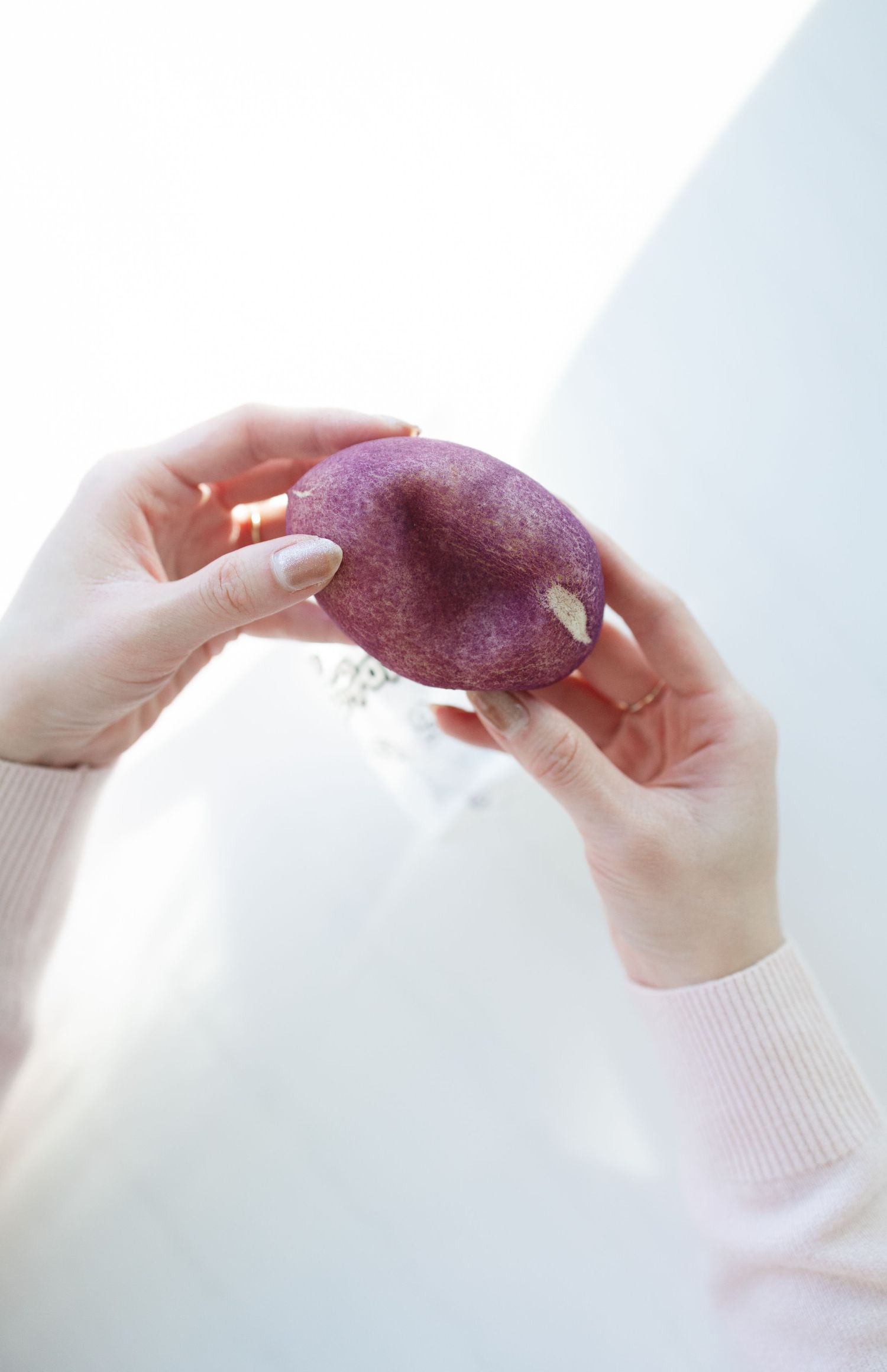 Hands holding and examining a purple sweet potato against a white background.