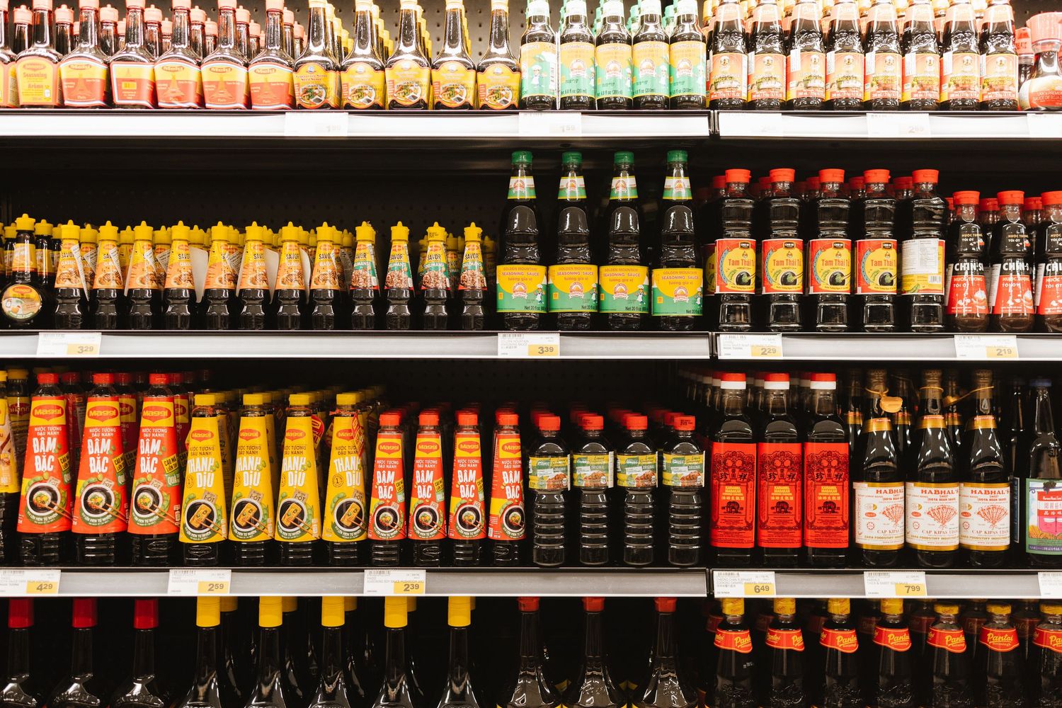 Colorful bottles of various sauces and beverages lined up on supermarket shelves.