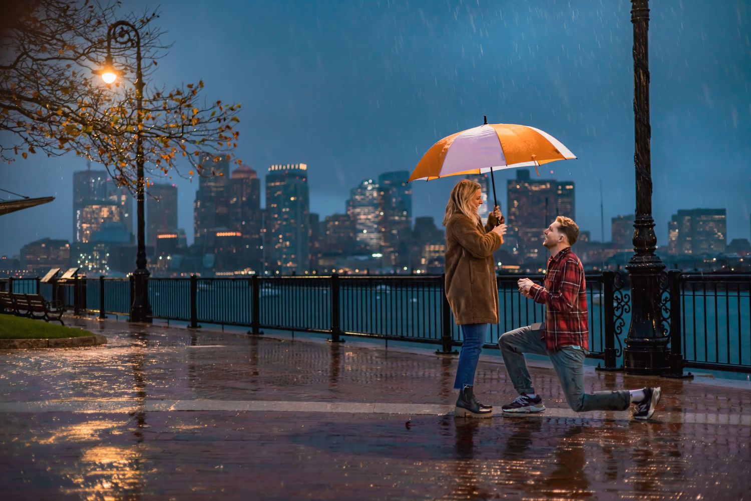 A romantic couple sharing a tender kiss in an urban setting with blurred city buildings in the background at dusk.