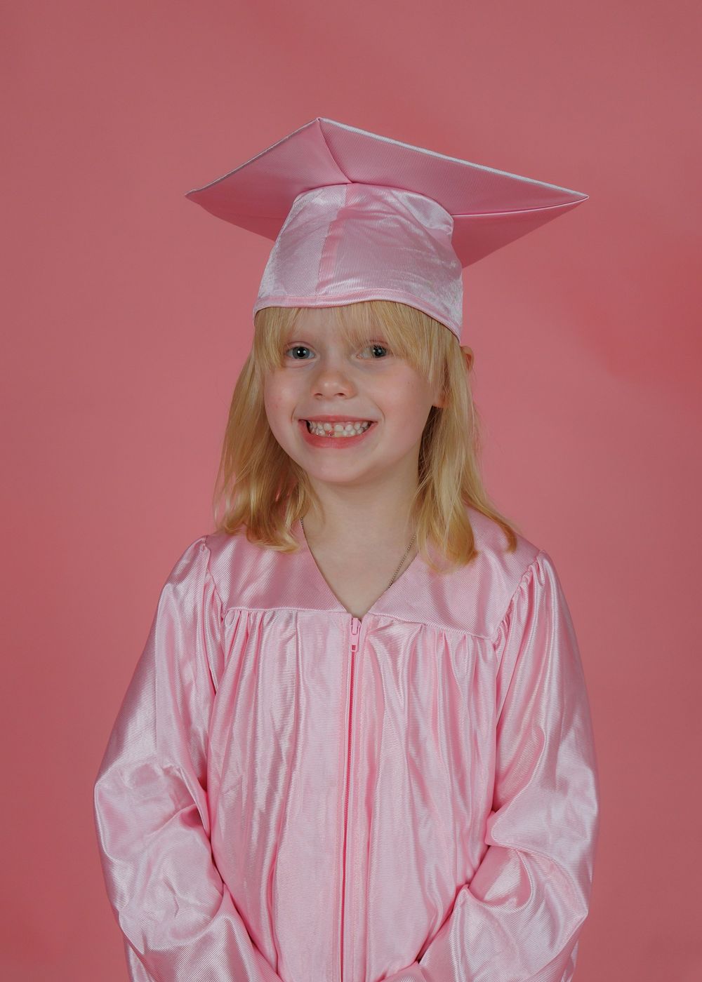 Graduate in pink cap and gown poses against pink background in a series of celebratory graduation photos.