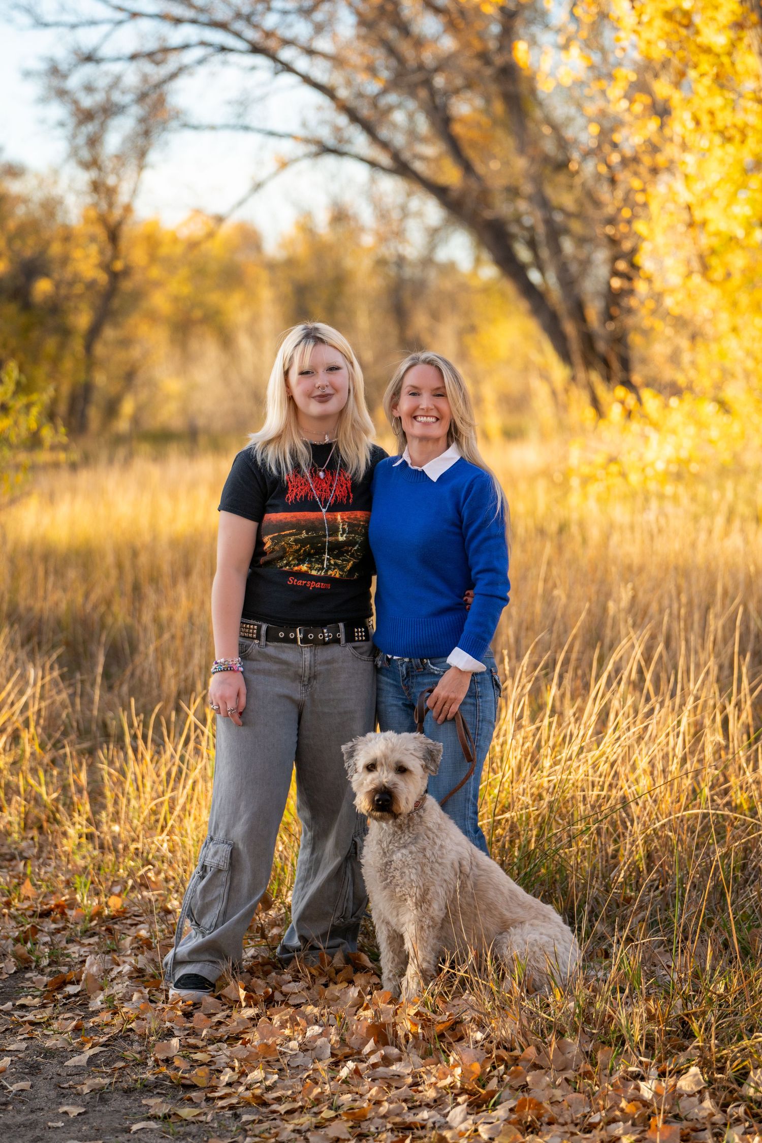 Two people and their white dog pose together in golden autumn field setting.