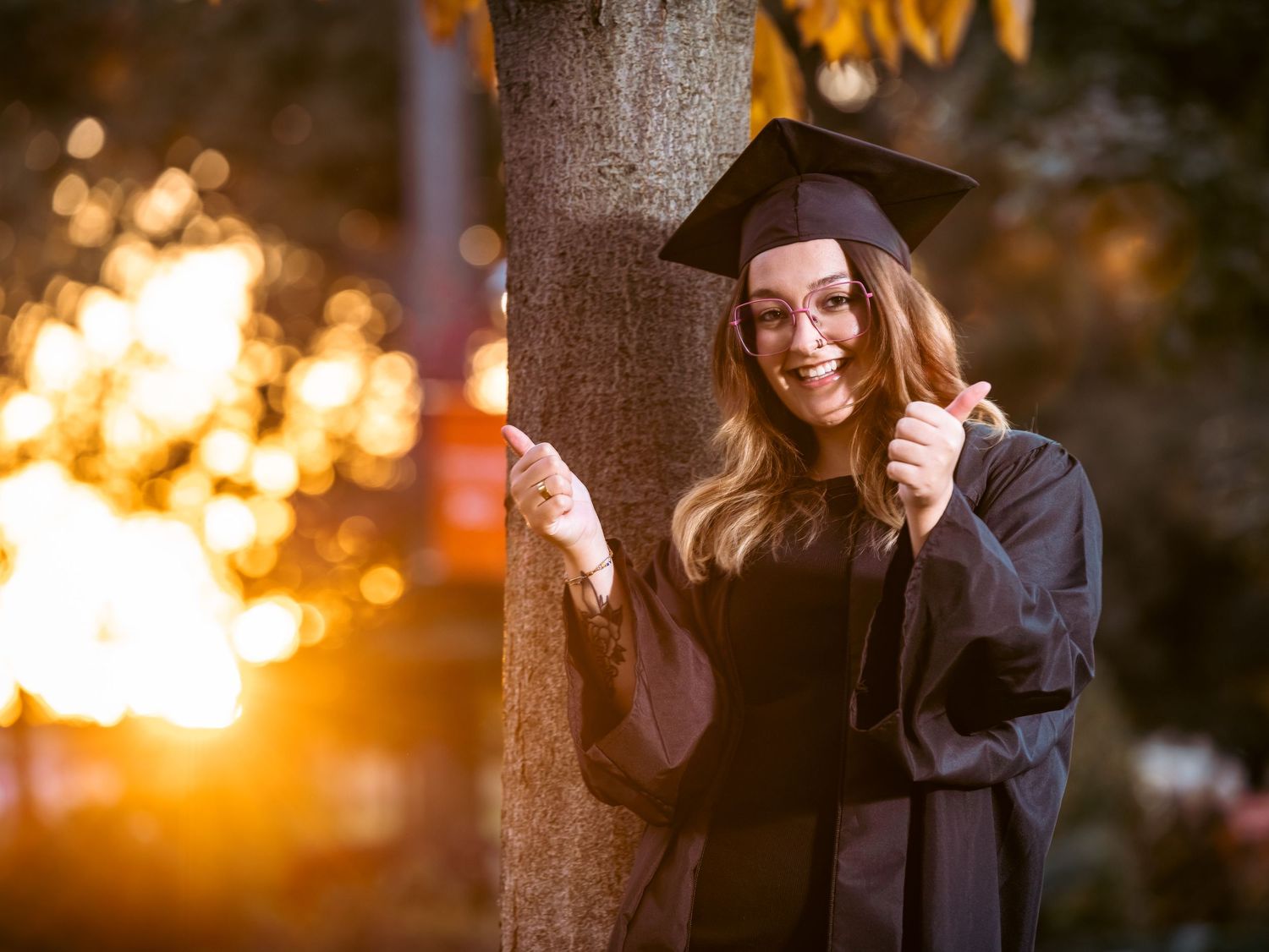 A graduation portrait against sunset with autumn trees in the background.