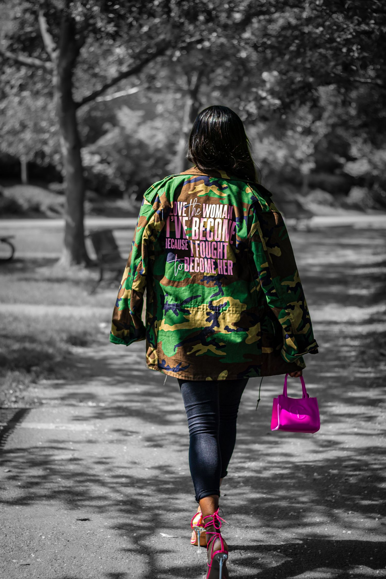 Black and white photo with color pop of pink bag and shoes, showing camo jacket with text from behind.