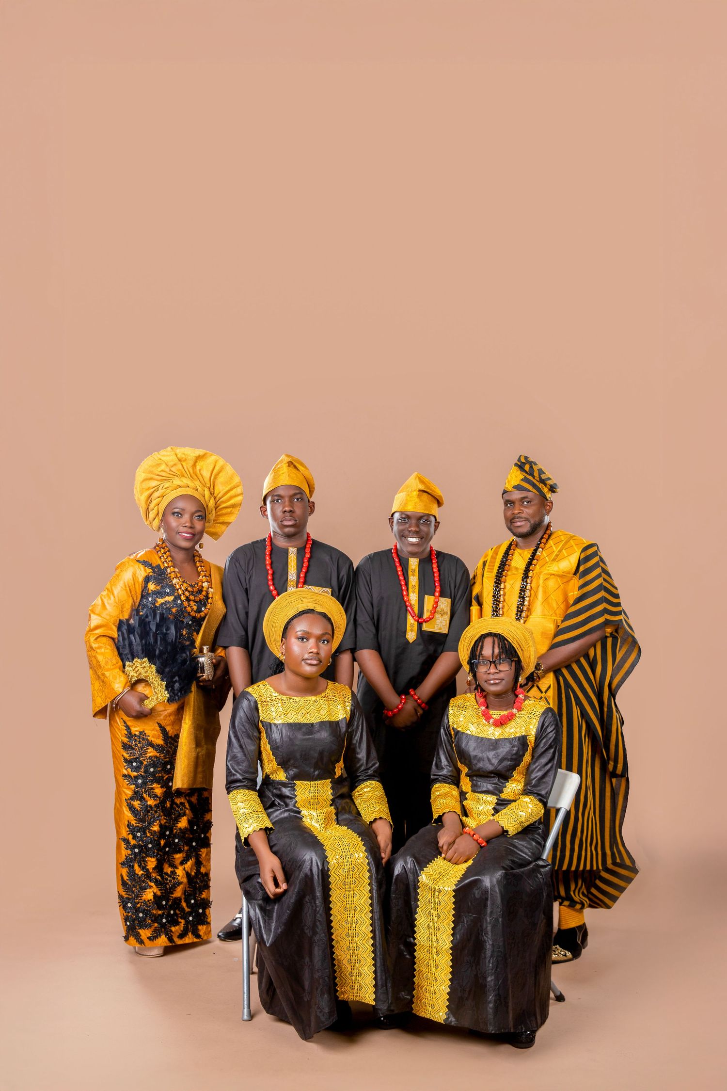 Group wearing vibrant yellow and black traditional African attire poses together against a neutral backdrop in studio setting.