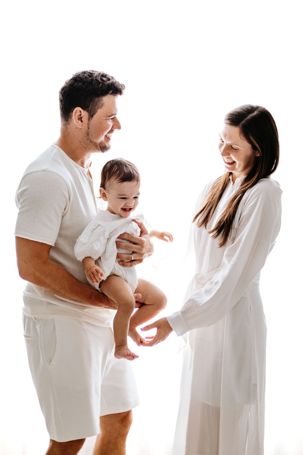 Family wearing white clothing shares joyful moment together against white background.