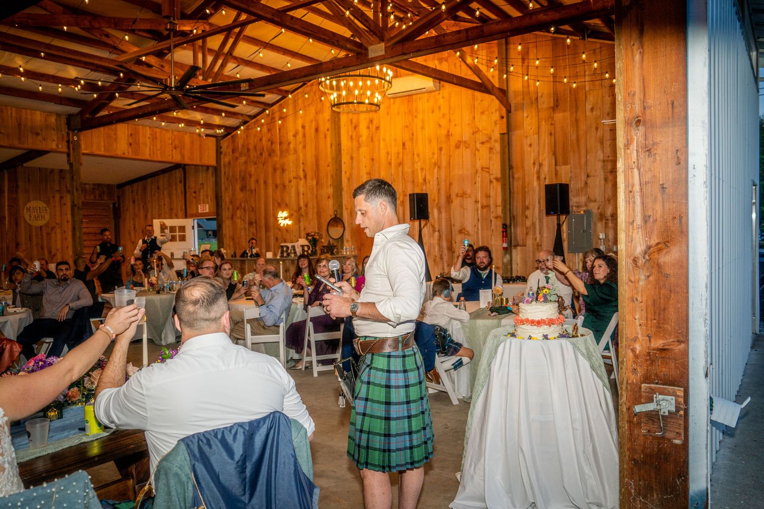 Wedding reception in rustic barn venue with wooden beams and warm lighting.