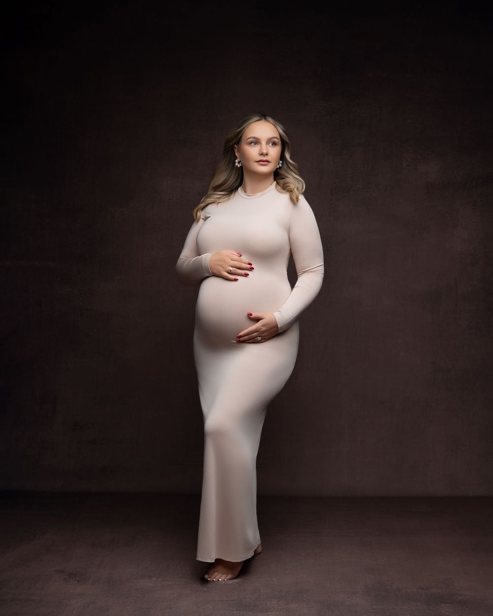 Studio maternity portraits showing a pregnant woman in a fitted beige dress against a dark backdrop.