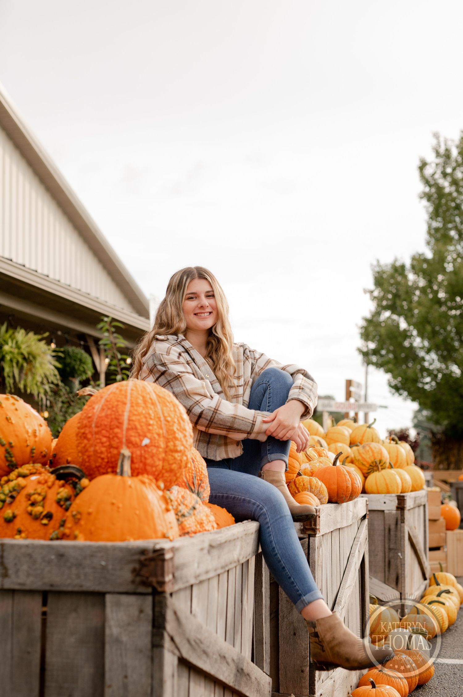 Someone poses on wooden crates filled with orange pumpkins at an autumn farm stand.