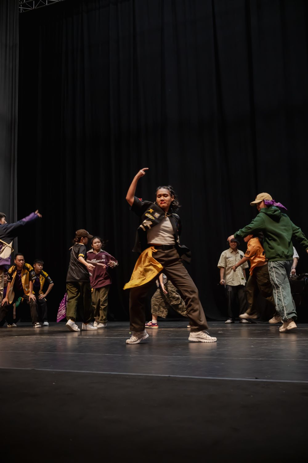 Group of dancers performing energetic hip hop routine on dark stage.