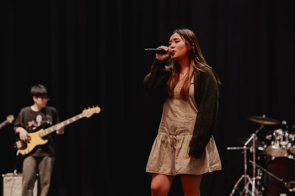 Singer performs on stage with band members playing instruments in background.