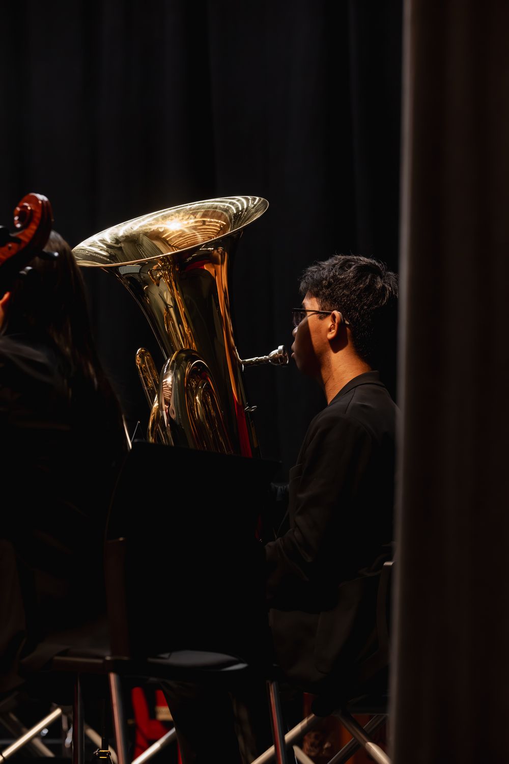 Musician plays large brass tuba instrument during dark stage performance.