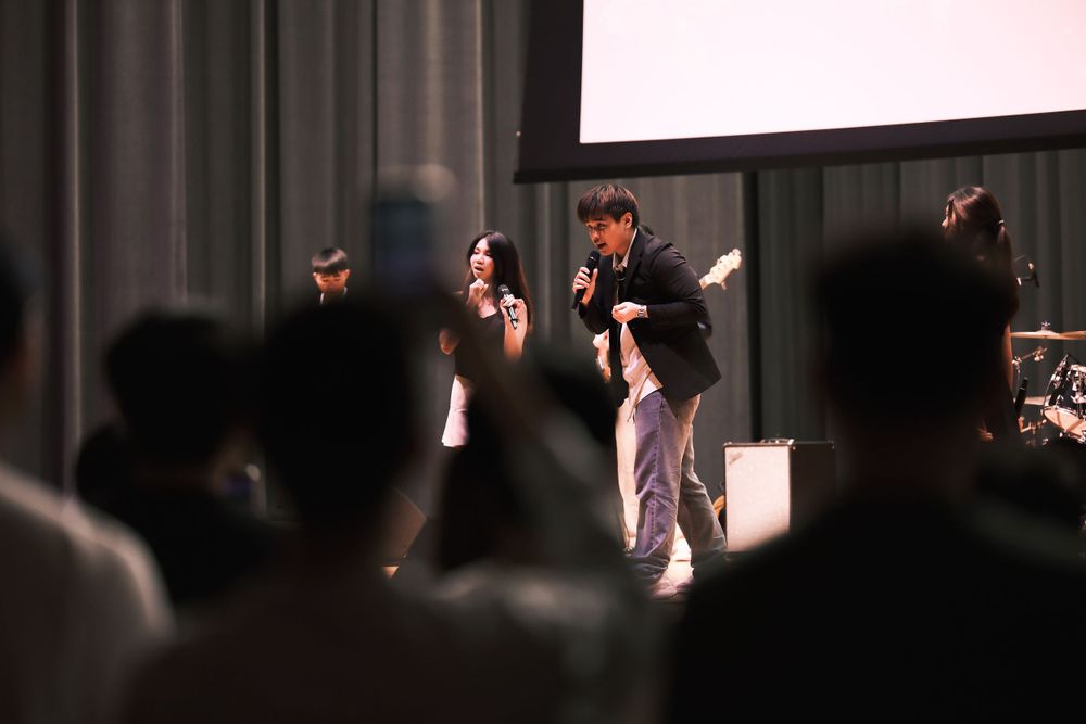 Performers on stage during a show with audience silhouettes in foreground.