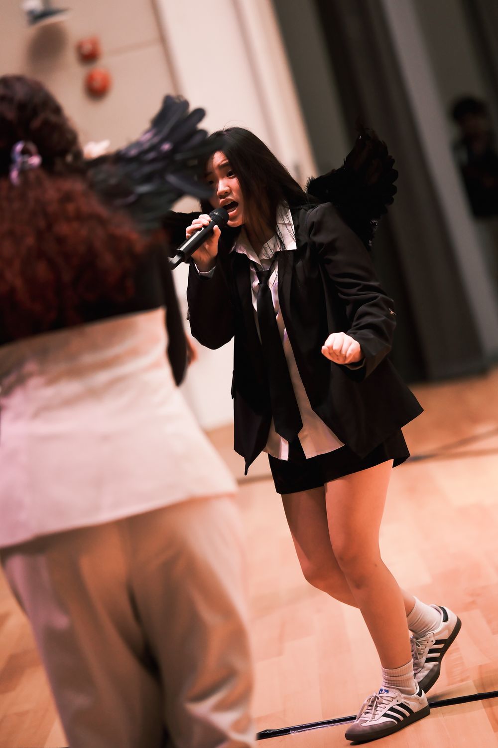 Energetic performer in black jacket singing into microphone on stage.