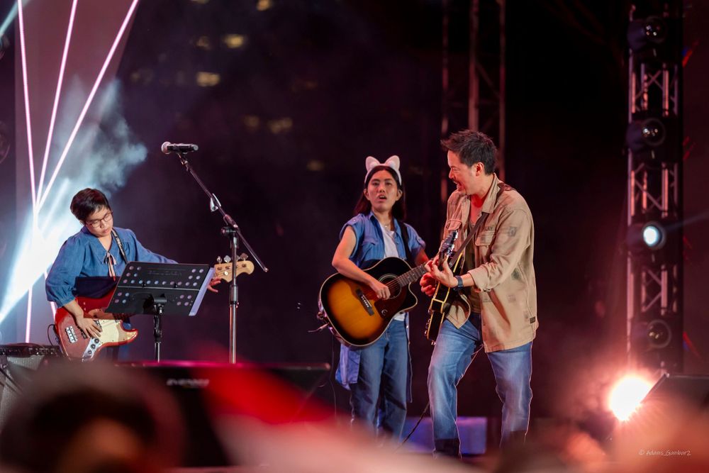 Musicians performing with acoustic guitars and instruments under stage lighting at live concert.