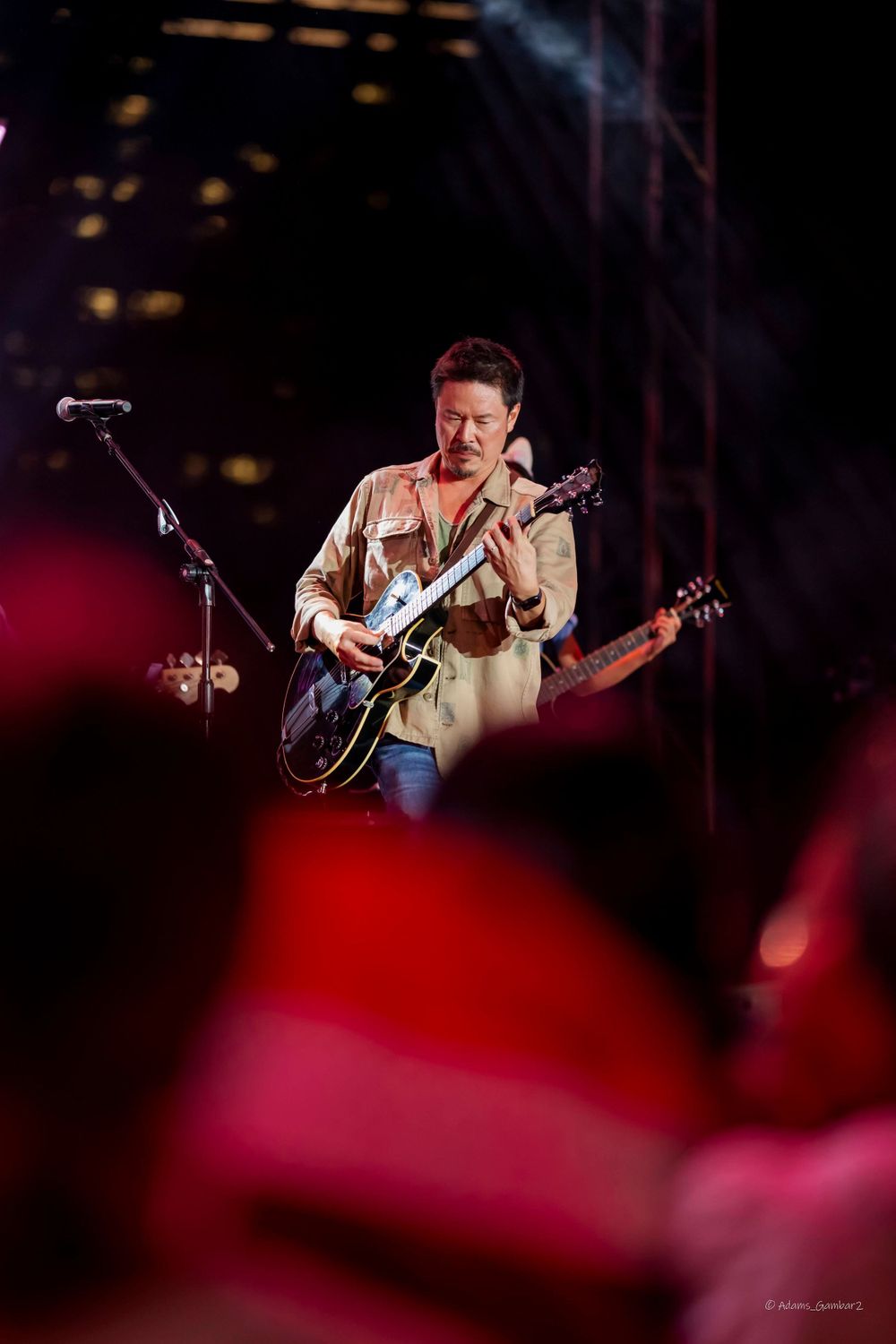 Guitarist playing electric guitar on stage with red stage lighting.