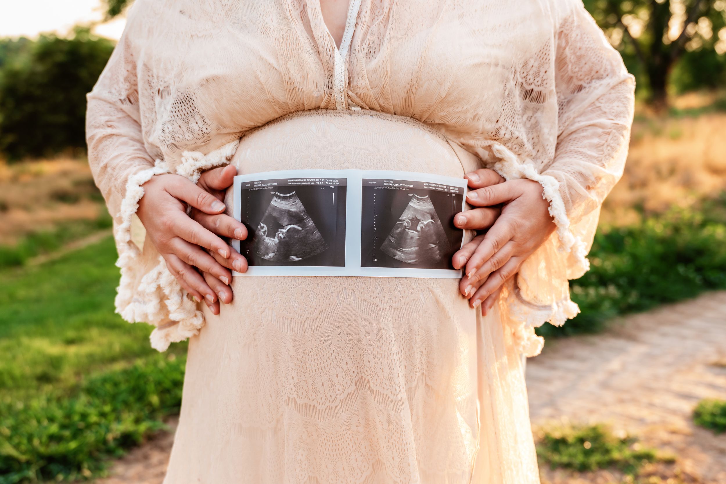 A person wearing a peach-colored dress holds up a sonogram photo in various outdoor poses during golden hour.
