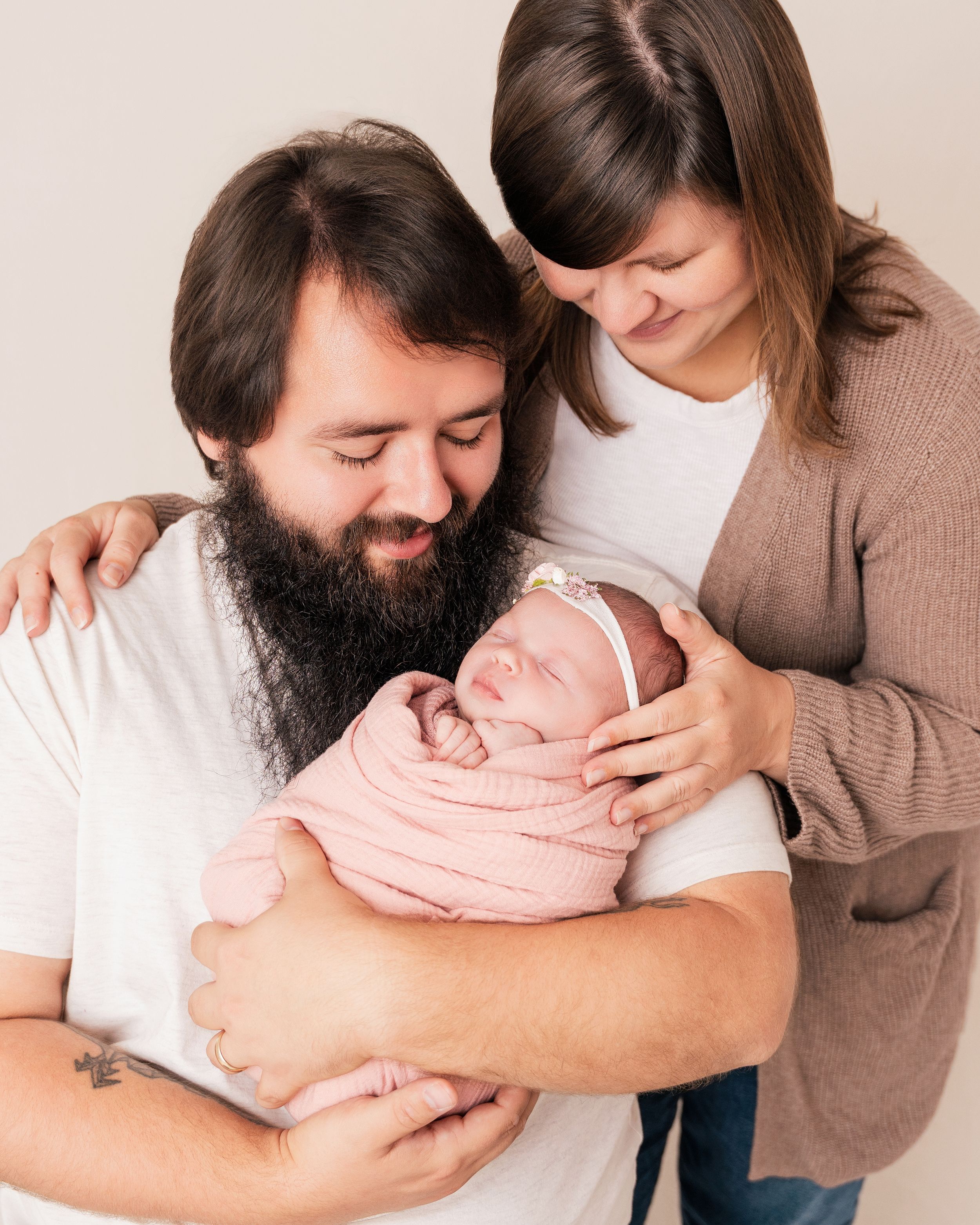 A couple holds their newborn baby wrapped in a pink blanket while sharing an intimate family moment together.