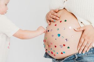 Toddler touching a pregnant mother's belly decorated with colorful heart-shaped gems and rhinestones.