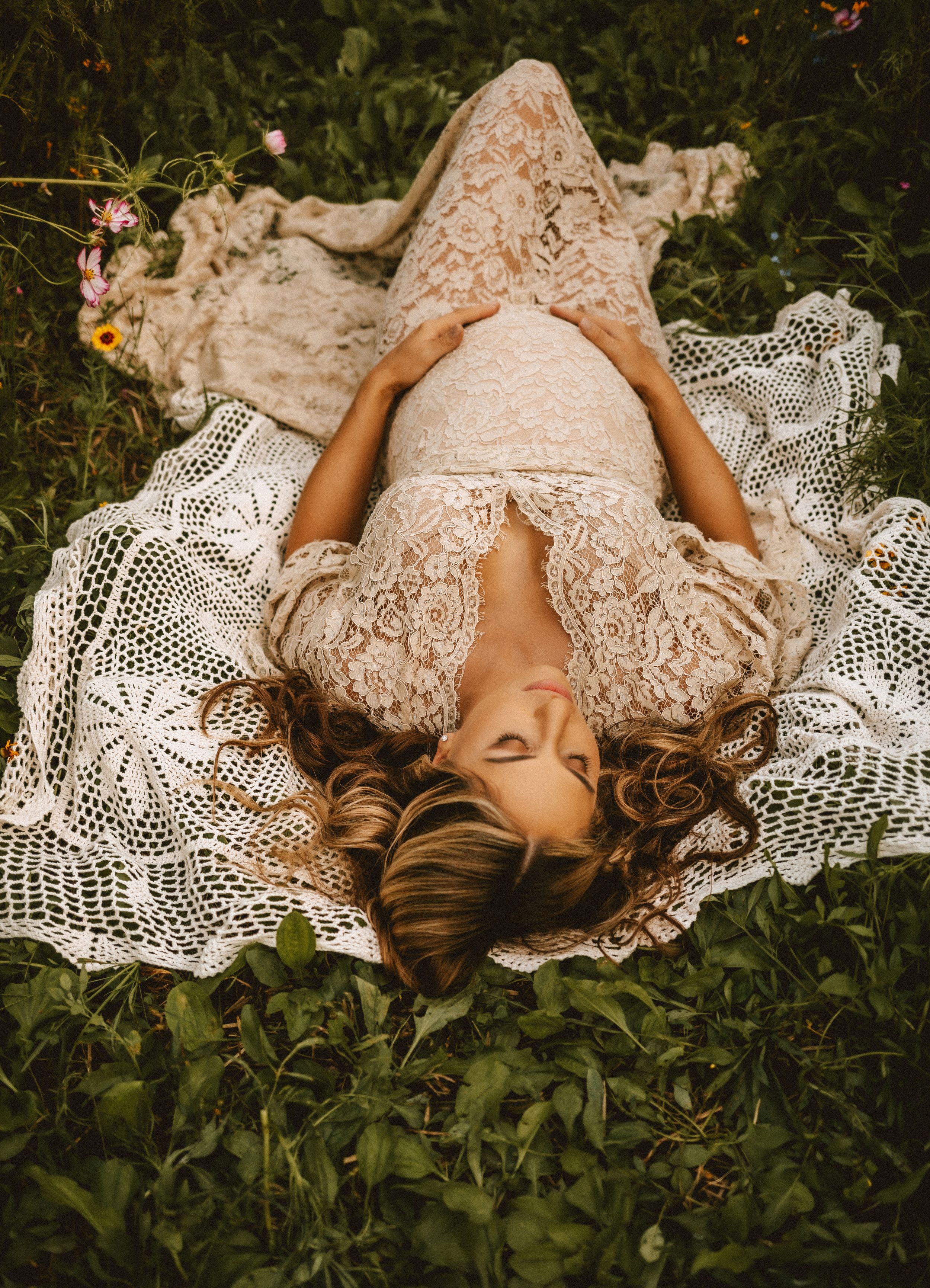 A dreamy outdoor photo series of someone laying in white lace among green foliage in multiple artistic poses.