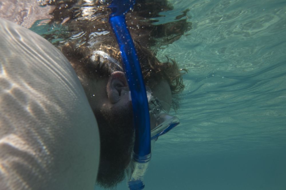 Underwater view of a snorkeler with a blue snorkel swimming in clear turquoise water.