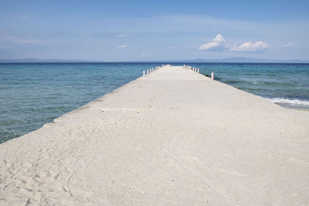 A long narrow white sand path extends into the turquoise ocean waters with wooden posts lining both sides.