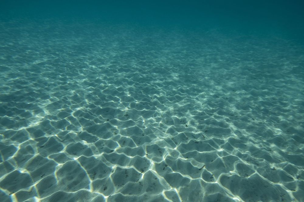 Rippling sunlight patterns dance across the sandy ocean floor beneath crystal clear turquoise waters.