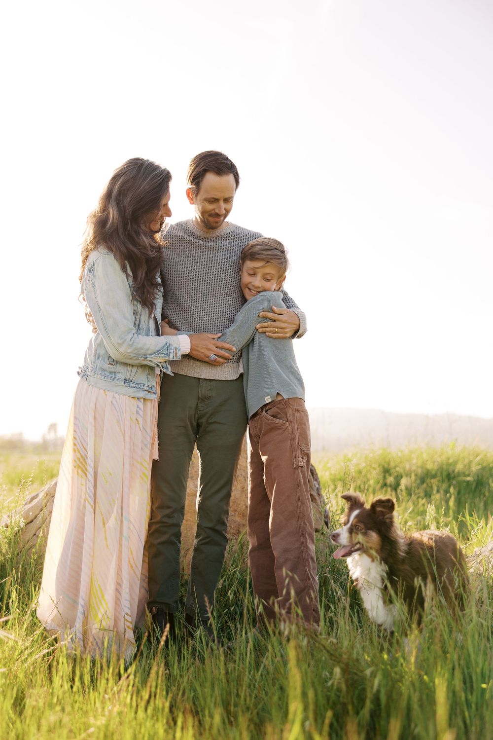 A family and their Australian Shepherd dog share tender moments together in a sunlit meadow during golden hour.