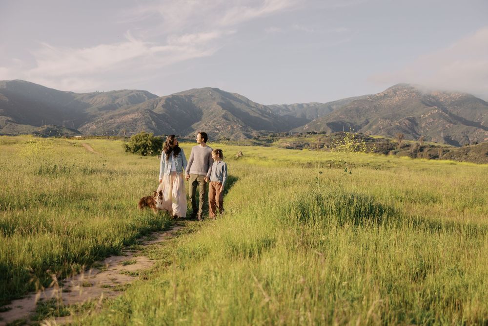 People and horses walk along a scenic mountain trail through green rolling hills on a sunny summer day.