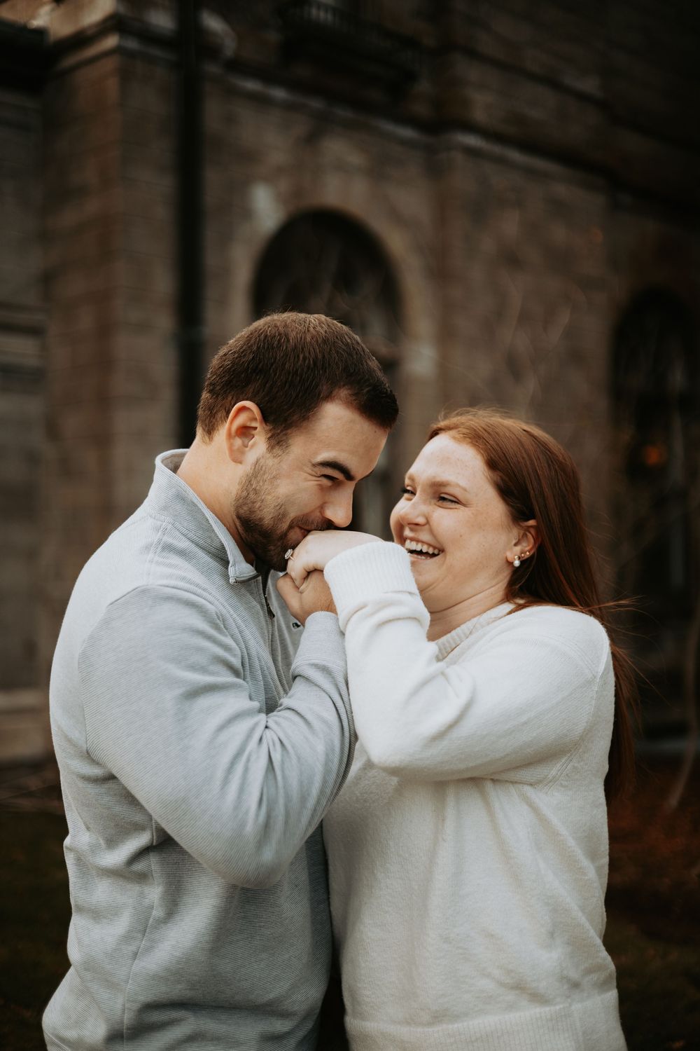 A couple in gray and white sweaters share intimate laughing moments in a series of candid outdoor photos.