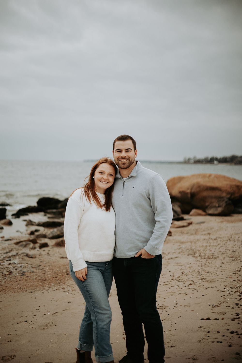 A couple shares a tender moment together on a rocky beach during an overcast day at the shore.