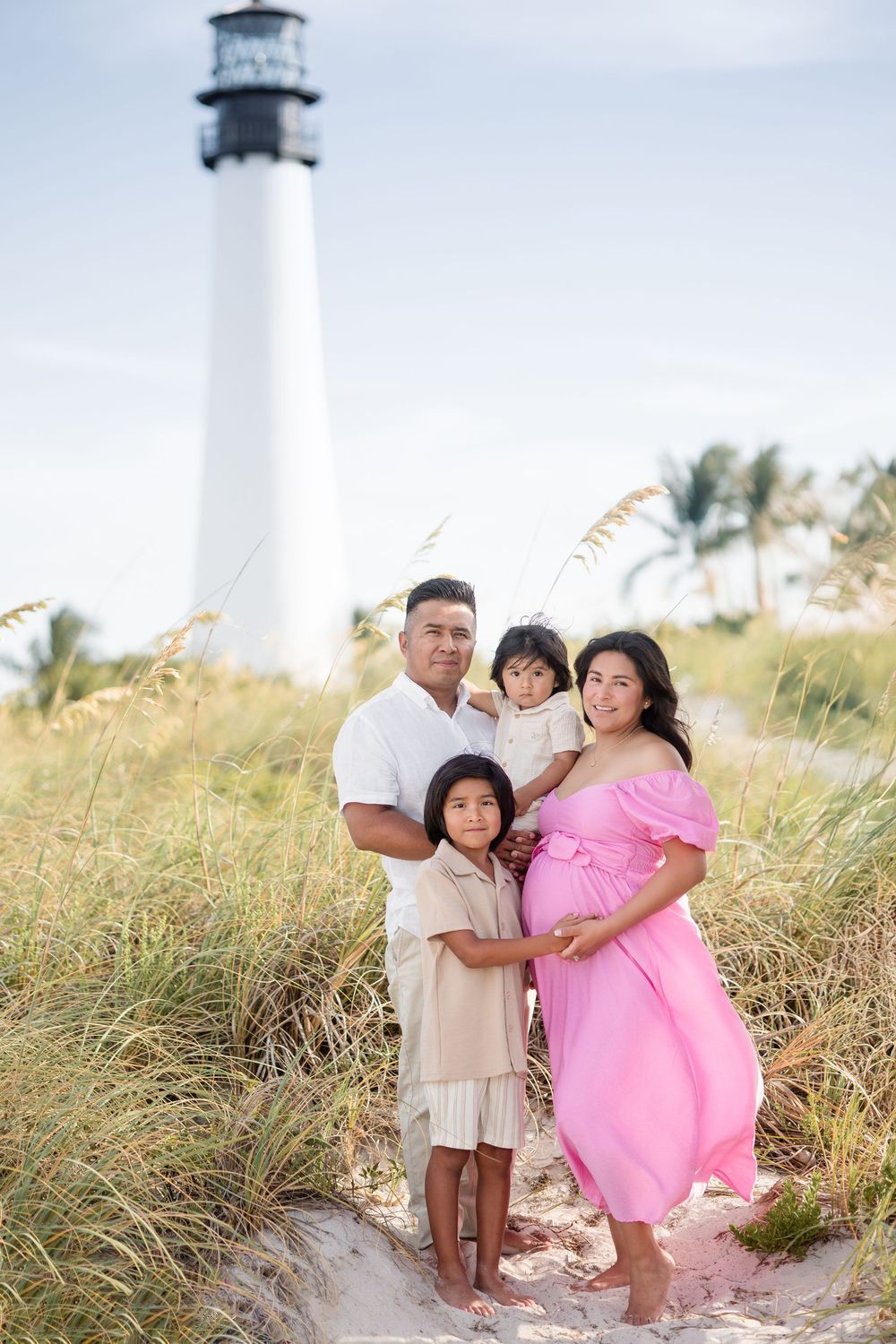 Pregnant woman in pink dress with family at Cape Florida lighthouse beach.
