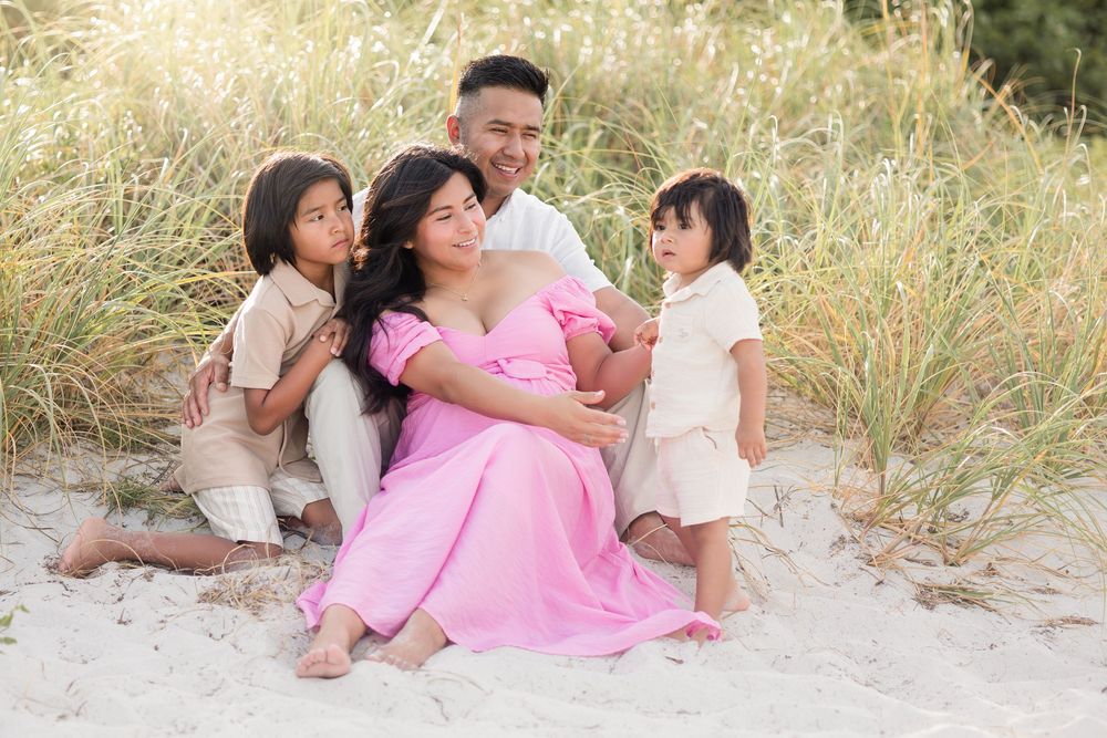 Happy family sitting together on sandy beach dunes in soft natural light.
