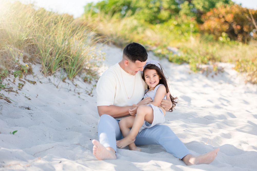 Father and daughter sitting together on sandy beach dunes sharing a sweet bonding moment.