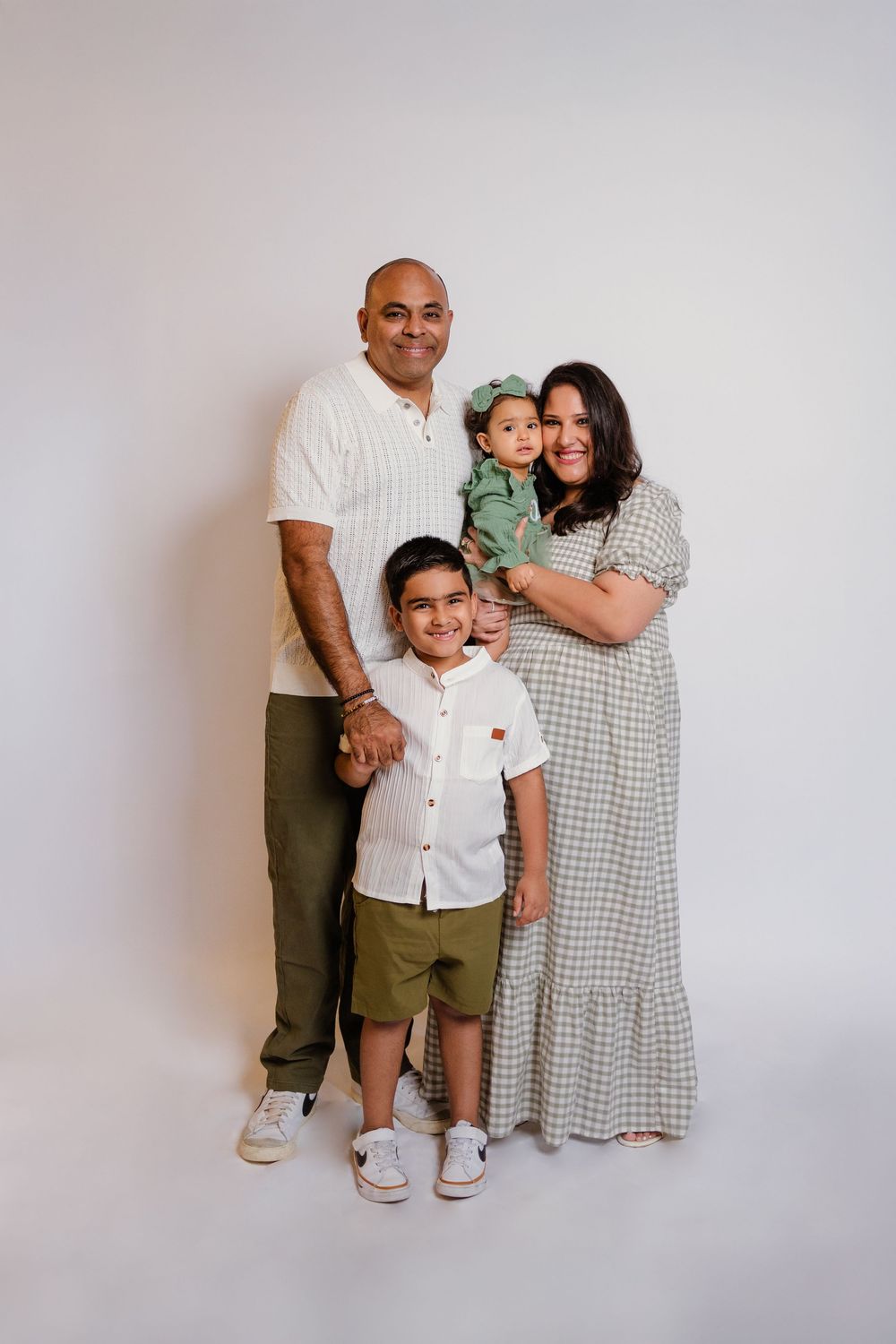 Smiling family portrait with two children in coordinated green outfits in studio.