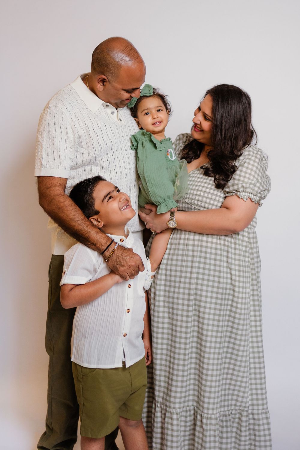 Family of four posing in green and white outfits against white studio backdrop.