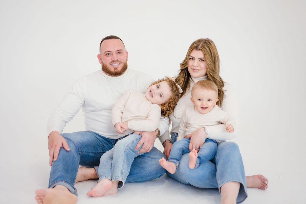 Happy family of four in matching white tops and jeans posing together on white background.
