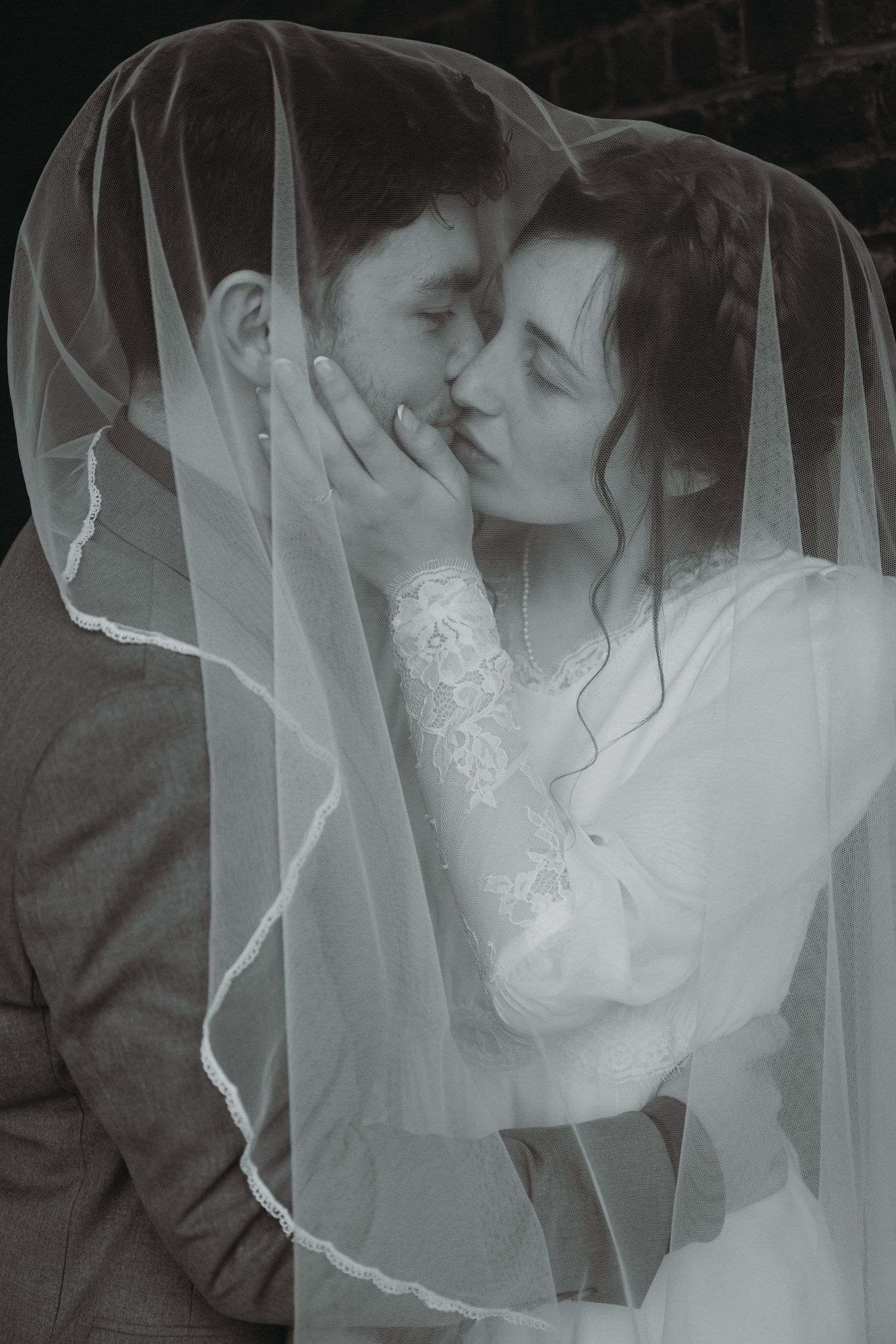 A romantic black and white photo of a couple sharing an intimate moment under a wedding veil.