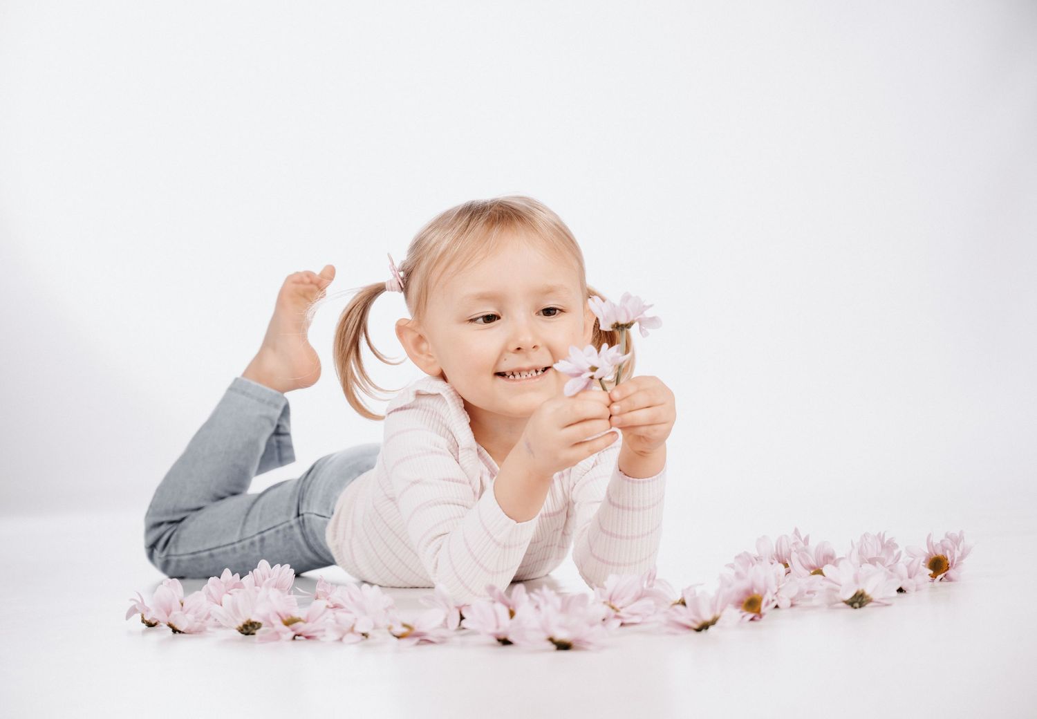 Mädchen auf weißem Fotostudio-Hintergrund in Gelsenkirchen-Hassel, Blumen in der Hand, umgeben von Blütenblättern