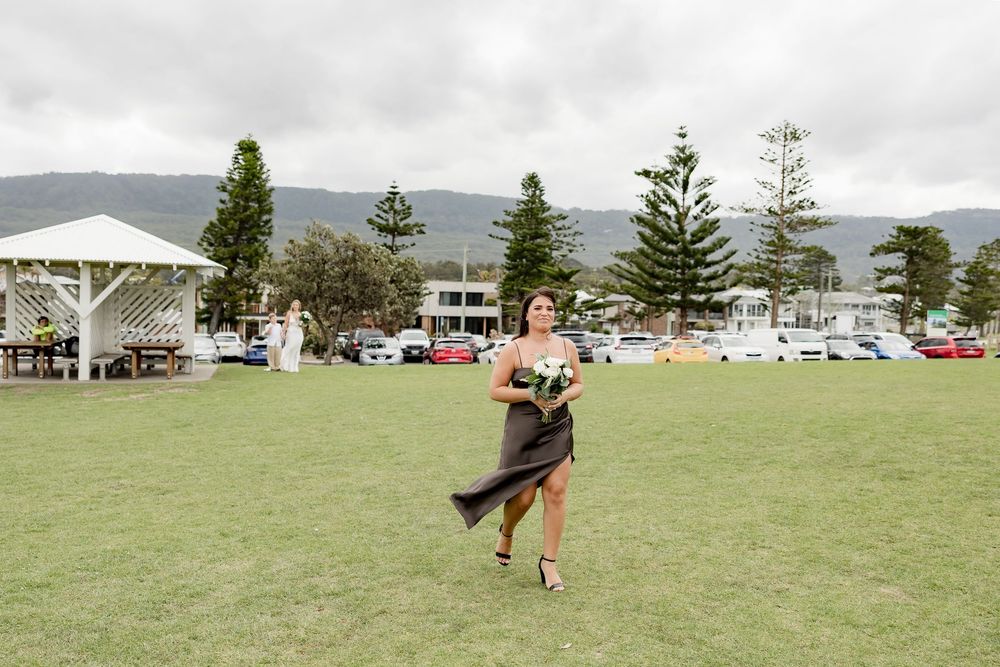 A person in a dress spins joyfully in a grassy field with mountains and buildings visible in the distance.