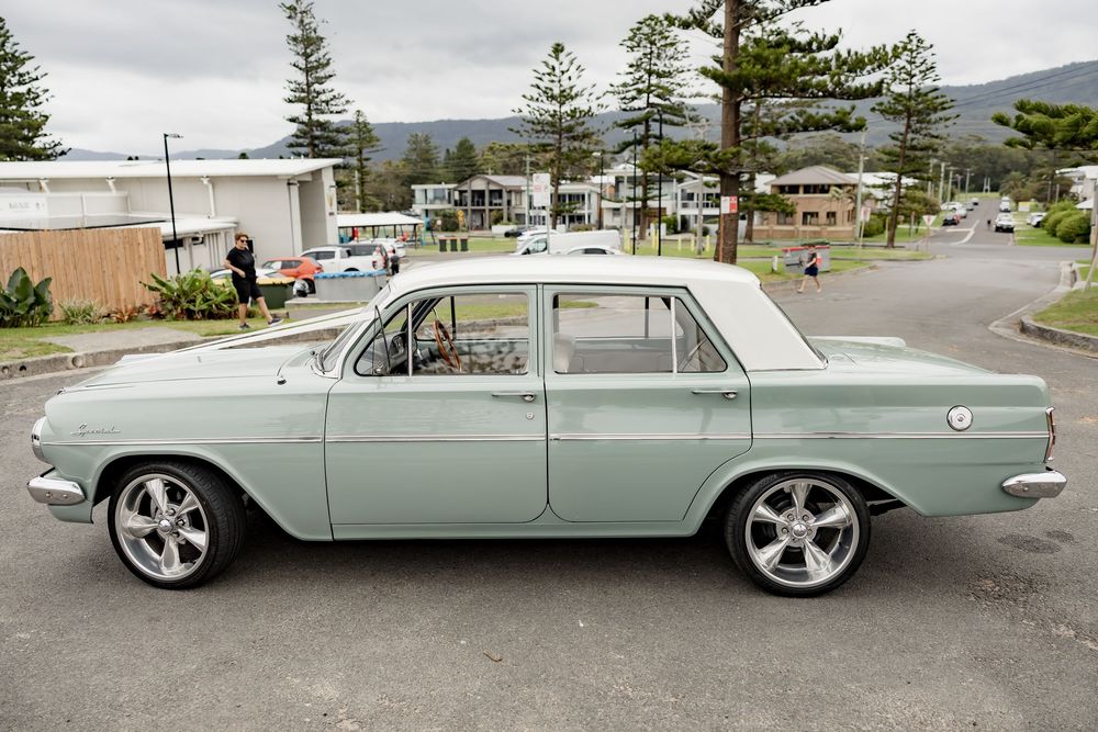 Classic mint green vintage car parked on a street with mountains in the background.