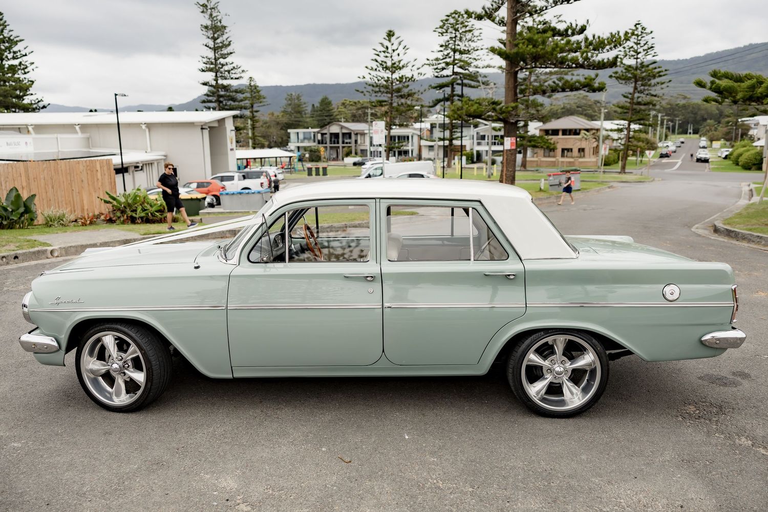 Classic mint green vintage car parked on a street with mountains in the background.