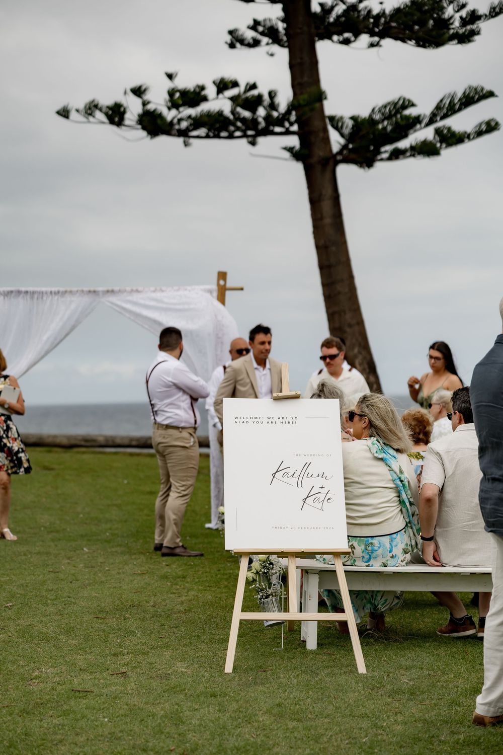 Wedding ceremony setup on a grassy hilltop with white signs and wooden easels under pine trees.