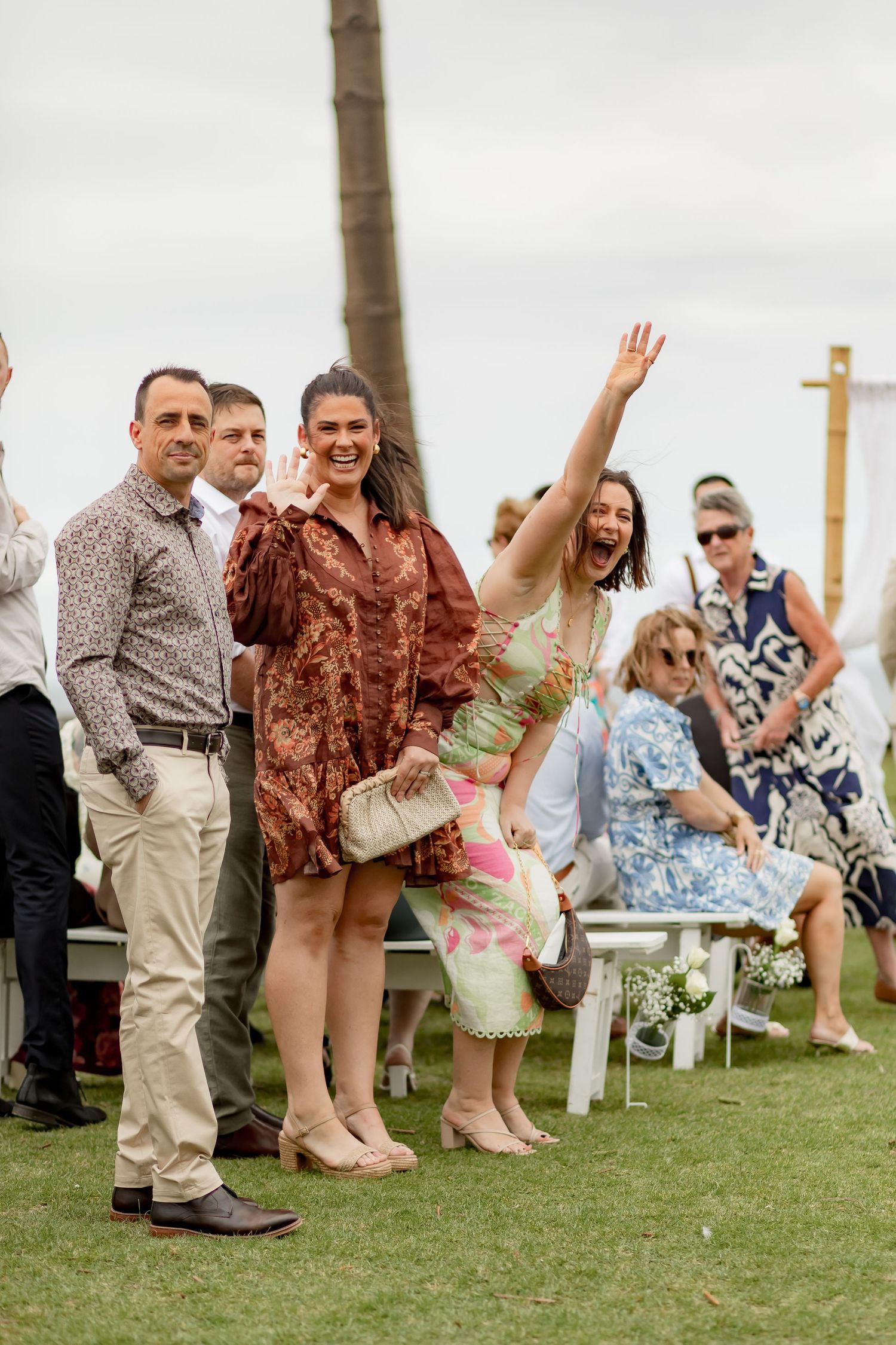 Wedding guests seated on white chairs on a grassy lawn during an outdoor celebration.
